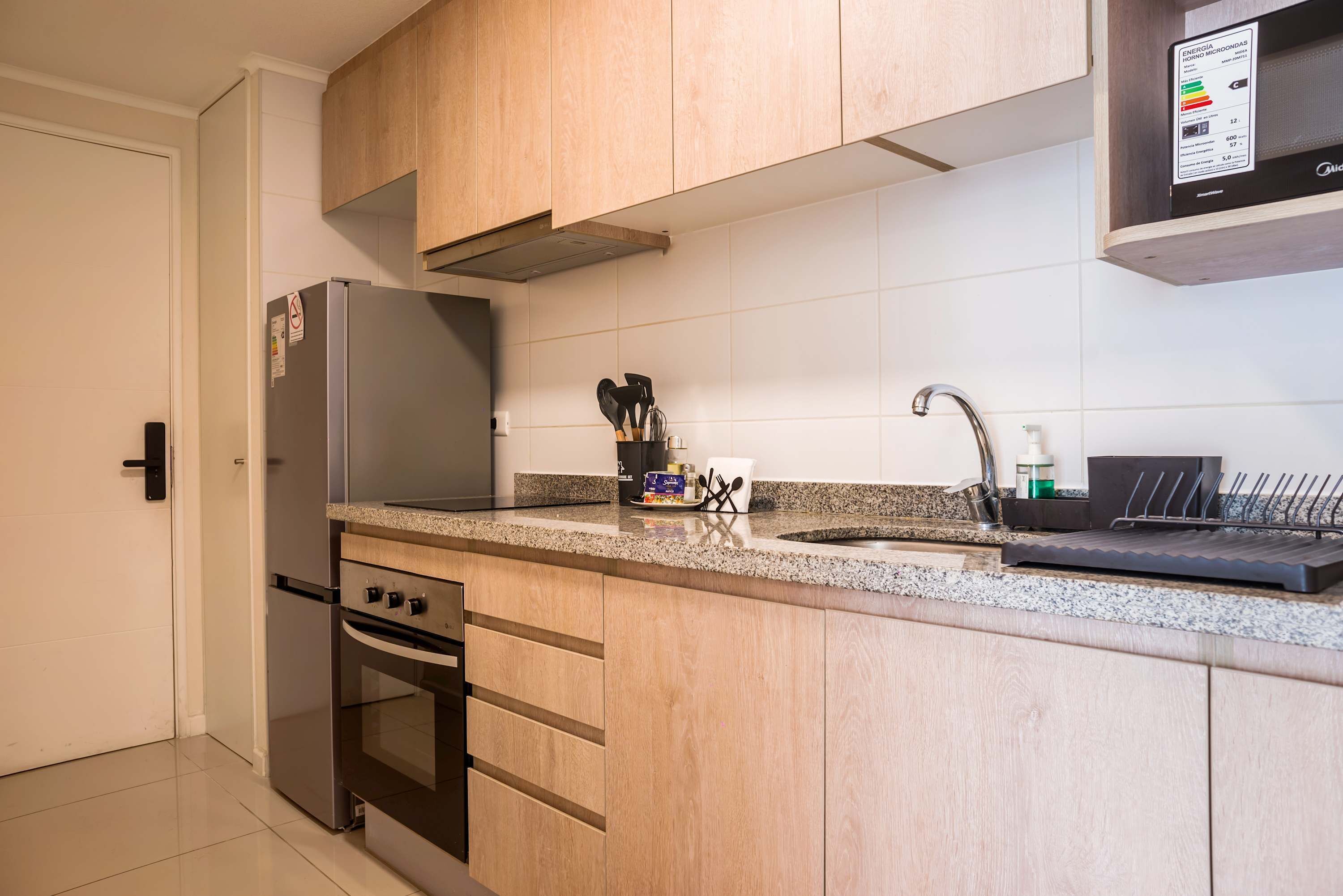 A modern kitchen with a stainless steel refrigerator, a built-in oven, a granite countertop, and a sink with a modern faucet.