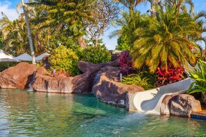 A pool with a water slide, surrounded by rocks and tropical plants. - Hale Akea by Alekona Kauai: Charming 3br Cottage w AC, Ocean Views, Spa, large yard (Koloa)