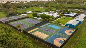 An aerial view of a sports complex with multiple tennis courts, surrounded by greenery and residential buildings.