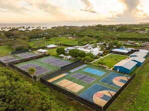 An aerial view of a sports complex with multiple tennis courts, surrounded by greenery and residential buildings.