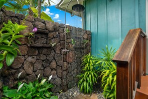 A stone wall with a showerhead, surrounded by tropical plants and a wooden staircase.