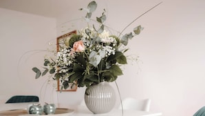 Mesa de jantar com um vaso de flores, duas maçãs e um prato branco.