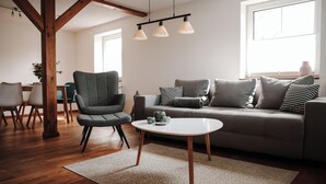 Uma sala de estar moderna com um sofá cinzento, uma poltrona a combinar, uma mesa de centro branca e soalho de madeira.