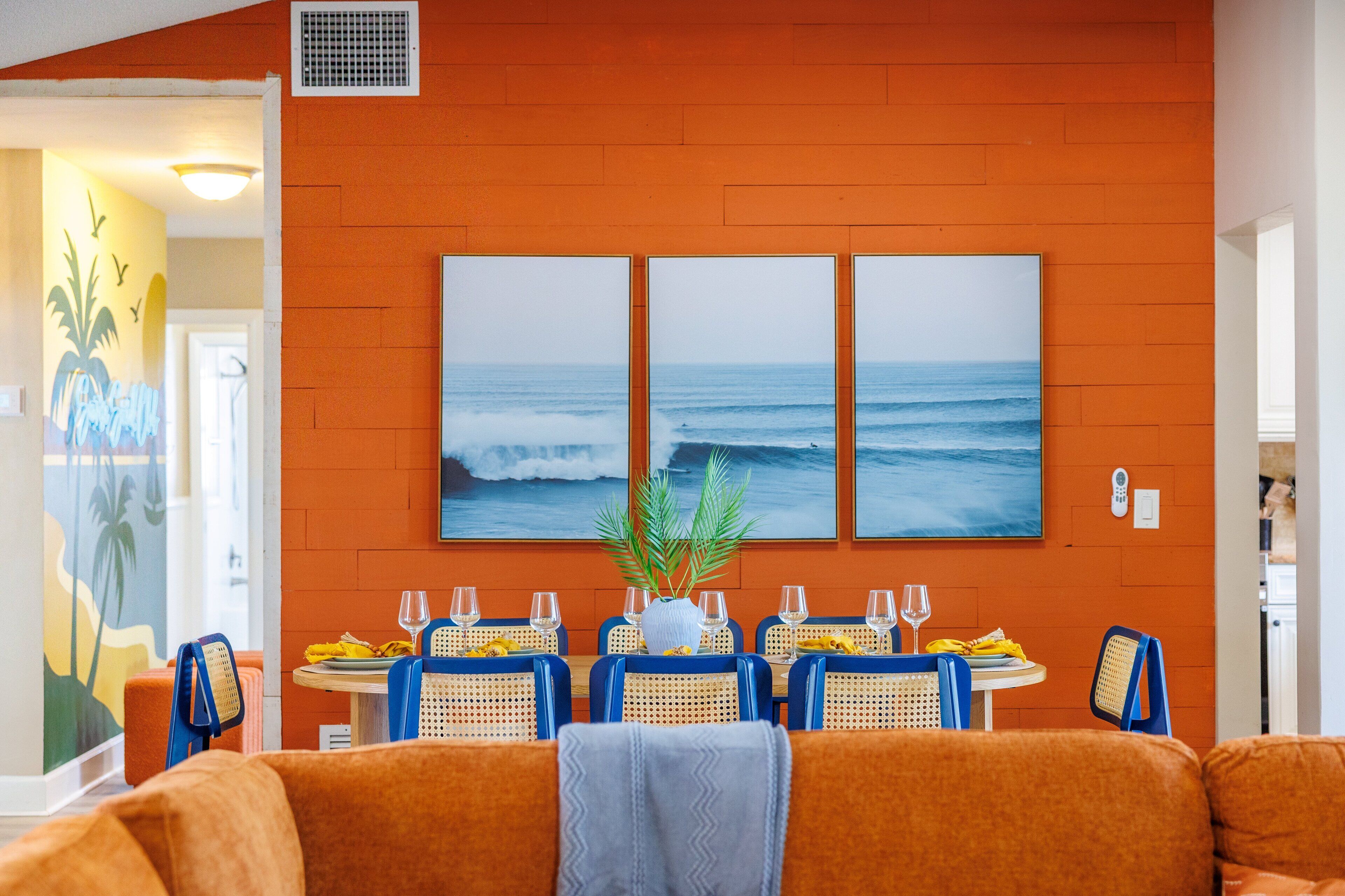 A dining area with a table set for four, a large ocean mural on the wall, and a plant centerpiece.