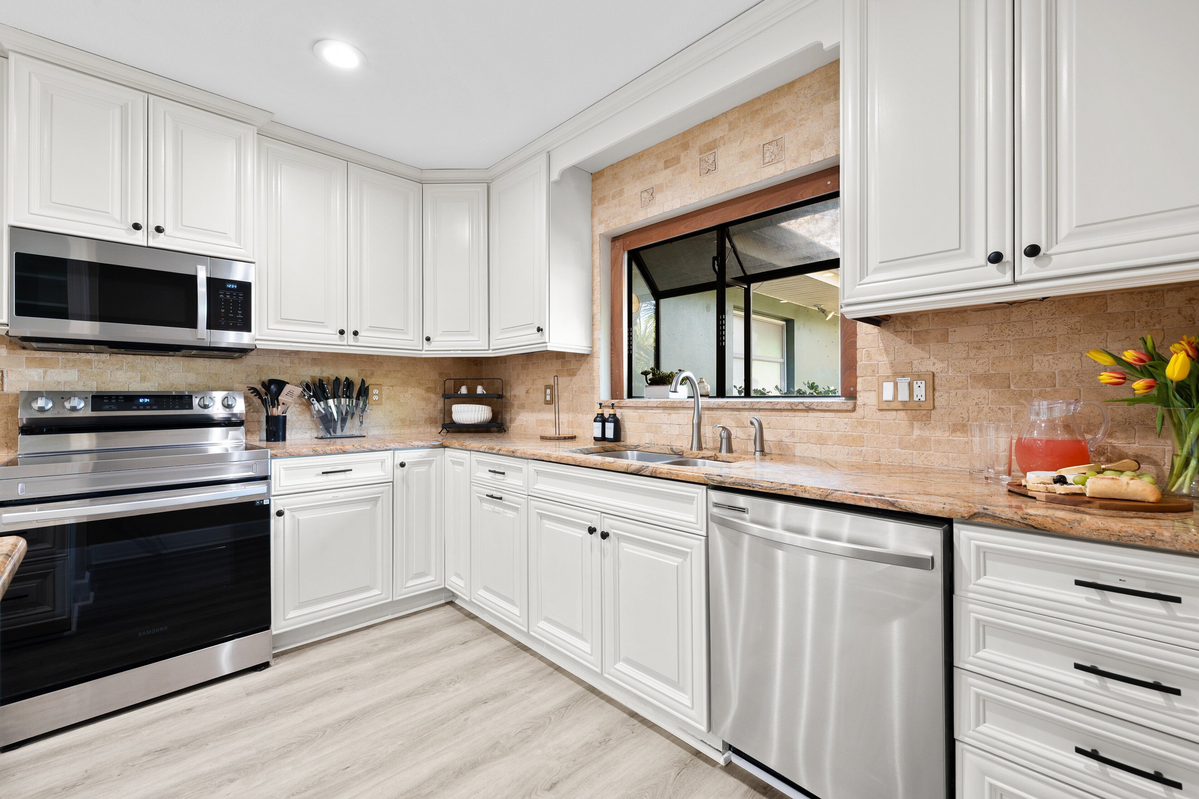A modern kitchen with white cabinetry, stainless steel appliances, and a large window.