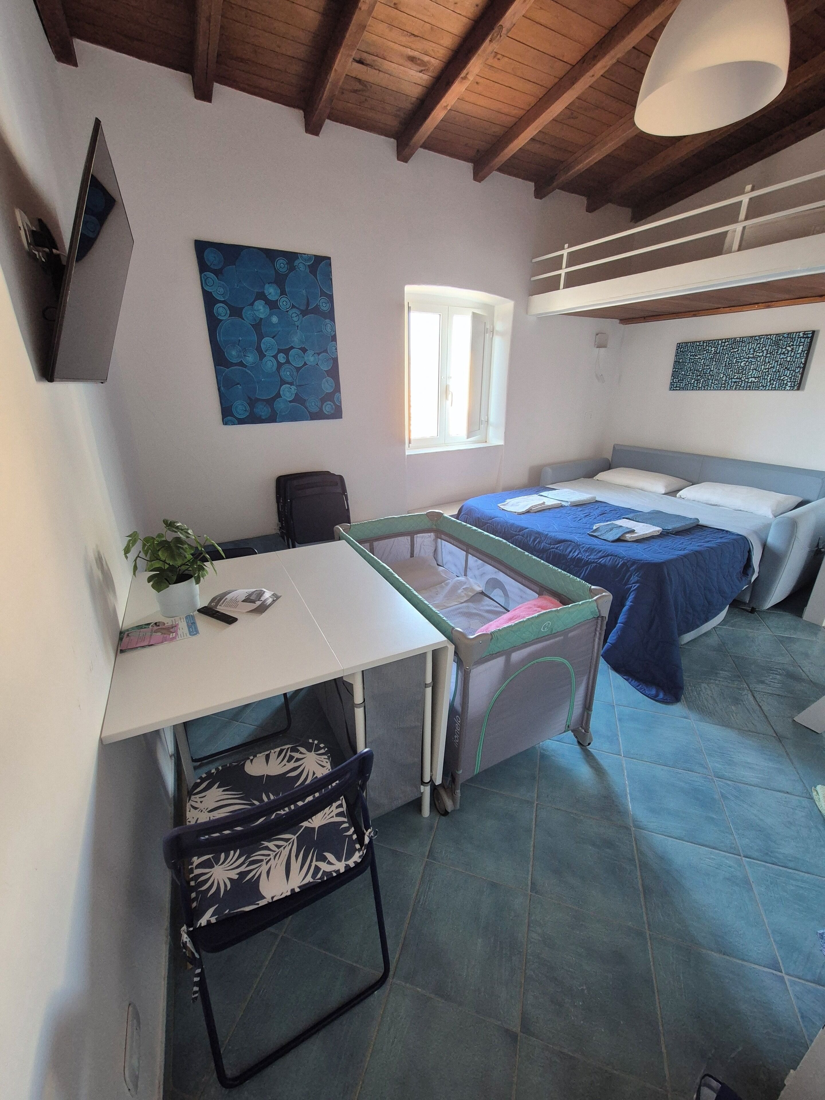 A room with a bed, a desk, a chair, a window, and a painting on the wall.
