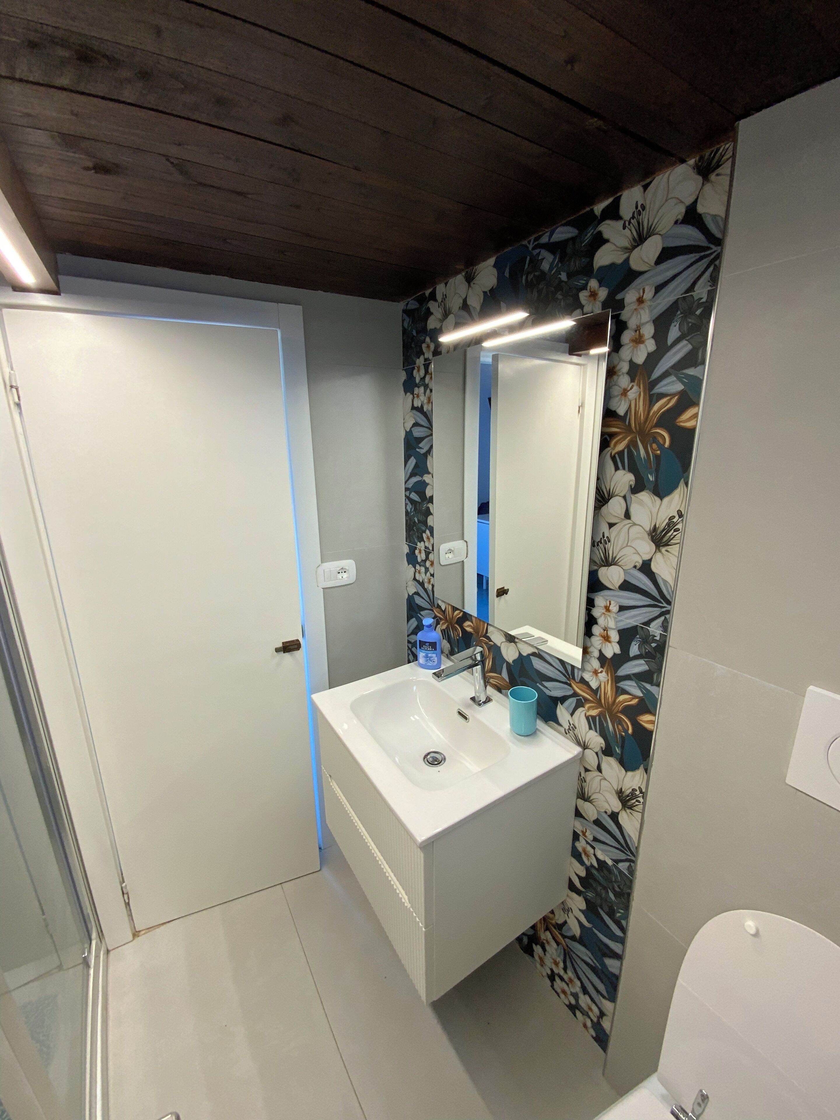 Un bagno con un lavandino bianco, uno specchio e carta da parati a motivi floreali.