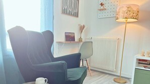 A modern living room with a dark green armchair, a small round table with a plate of food, a floor lamp, and a radiator.