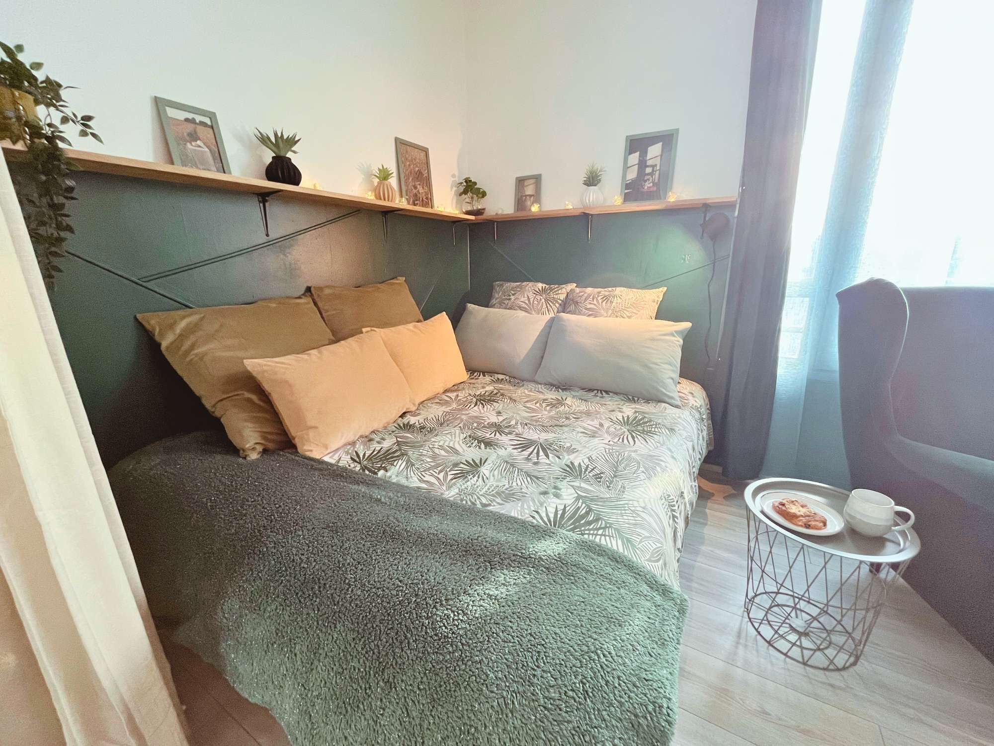 A modern bedroom with a bed, pillows, a small side table, and a shelf with decorative items.