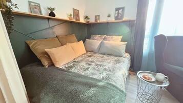 A modern bedroom with a bed, pillows, a small side table, and a shelf with decorative items.