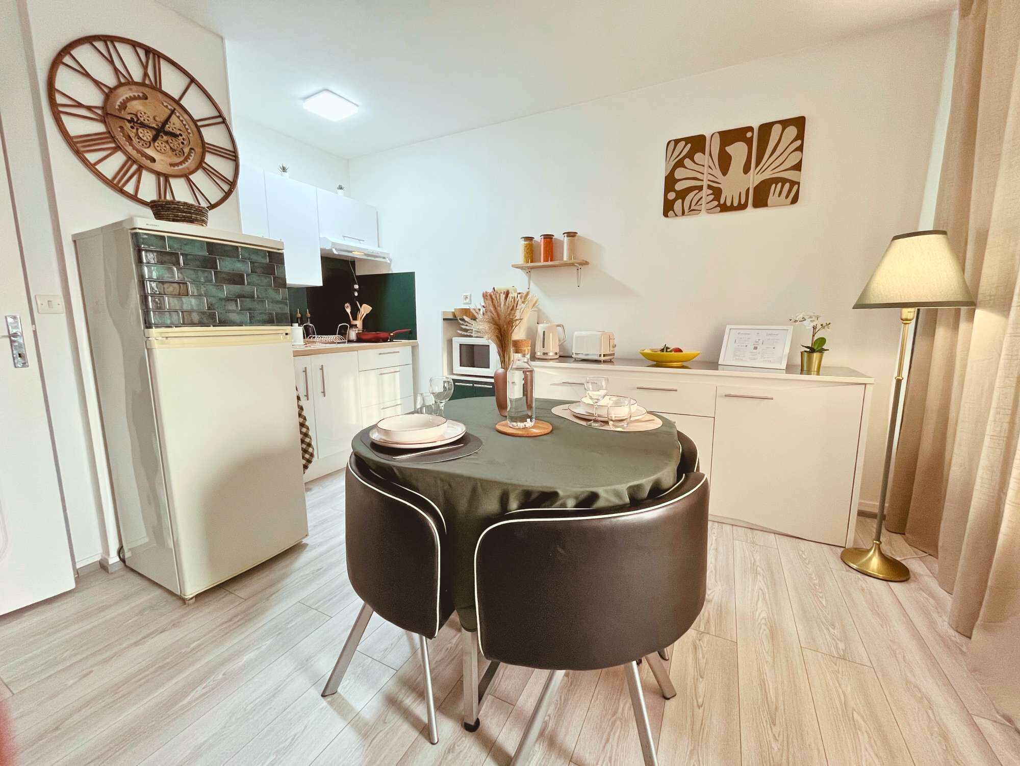 Una cocina compacta con comedor, que incluye un refrigerador moderno, un reloj y una decoración minimalista.