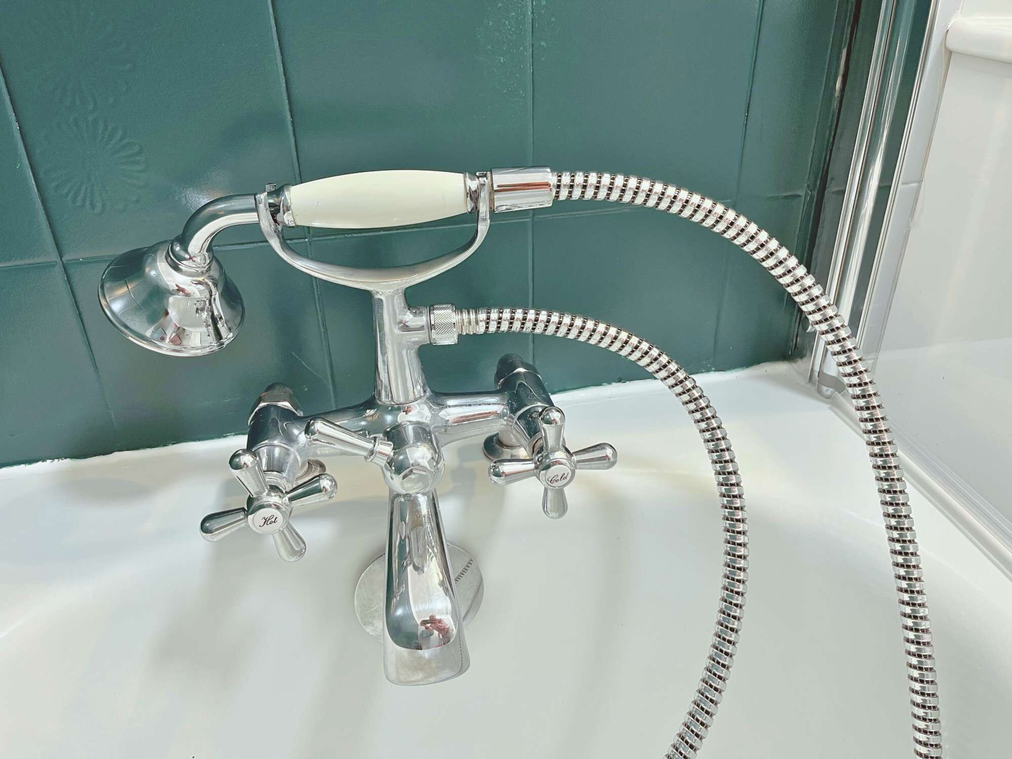 A chrome bathroom fixture with a handheld showerhead and multiple faucets.