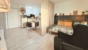 A modern apartment with a dining area, kitchenette, and a living room with a sofa and a bed.