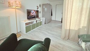 A modern living room with a flat-screen TV, a floor lamp, a white cabinet, and a green sofa.