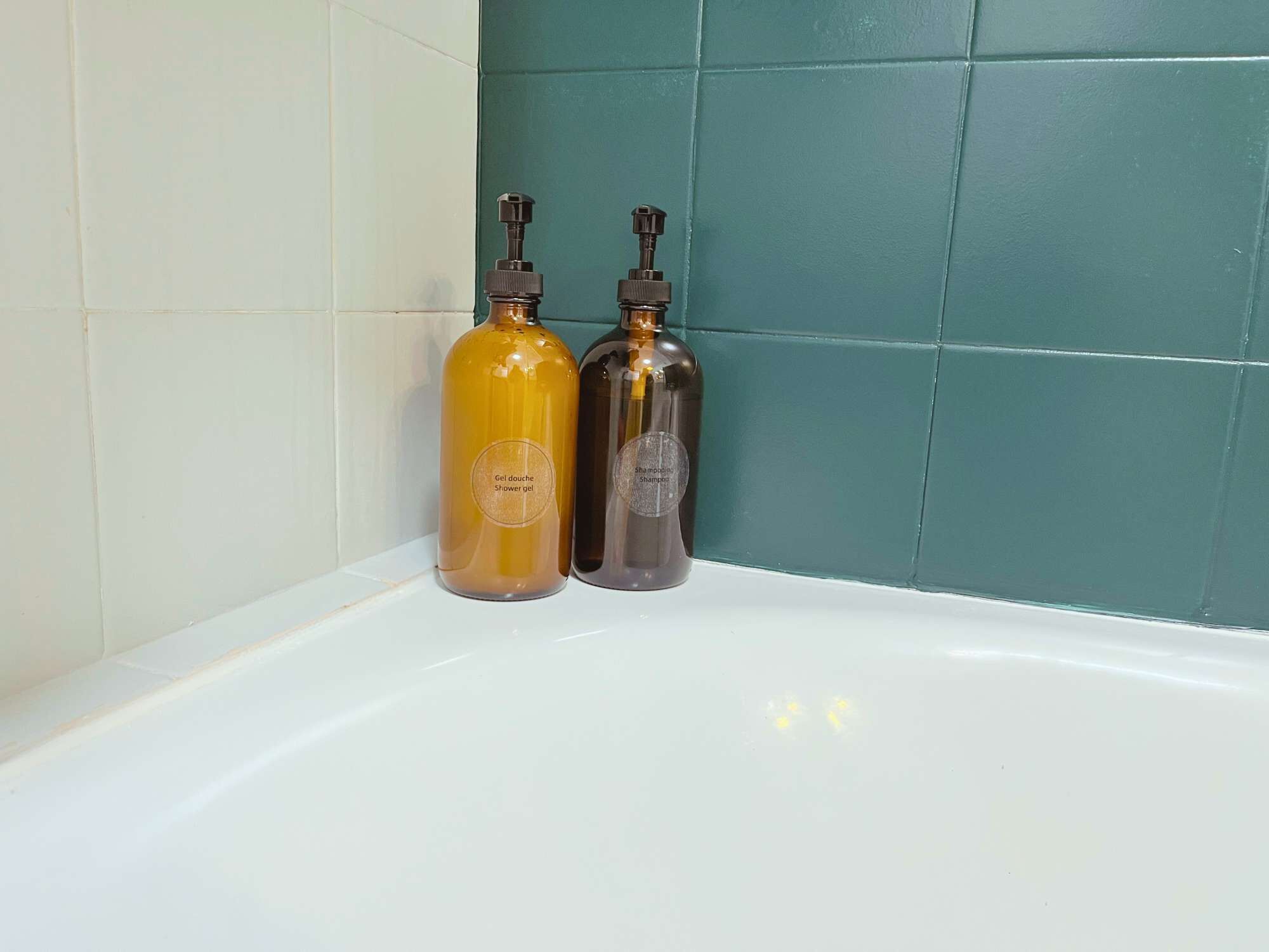 Deux bouteilles de gel douche et de shampoing sur une baignoire blanche.