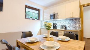 A modern kitchen with white cabinets, a stone backsplash, and a wooden dining table set with white bowls and plates. - Apartment in Harrachov With Barbecue (Harrachov)