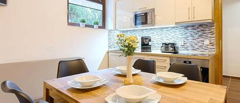 A modern kitchen with white cabinets, a stone backsplash, and a wooden dining table set with white bowls and plates.