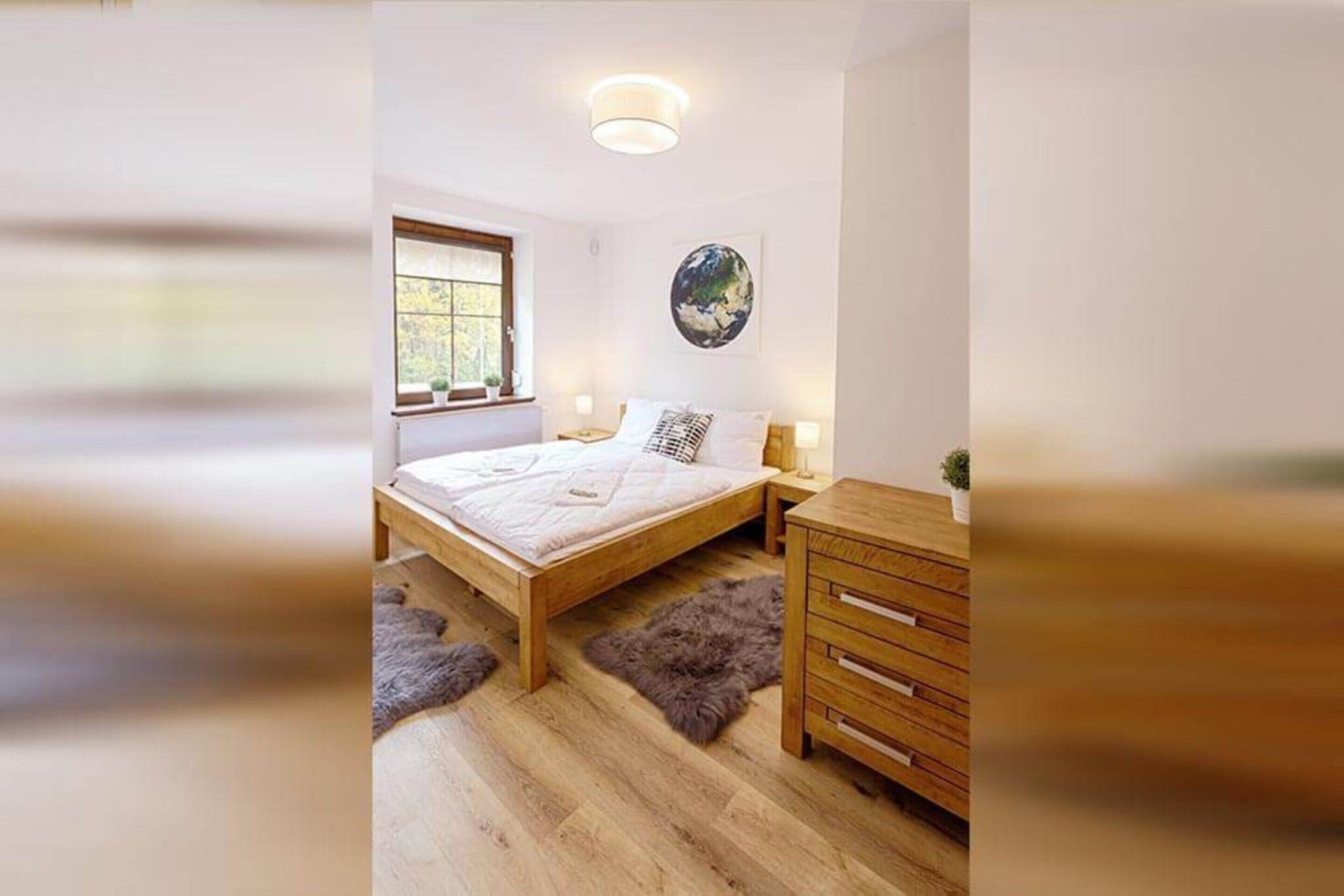 Ein Schlafzimmer mit einem hölzernen Bett, einem Nachttisch, einer Kommode, einem Globus als Kunstwerk und einem Fenster mit Blick auf Grünflächen.