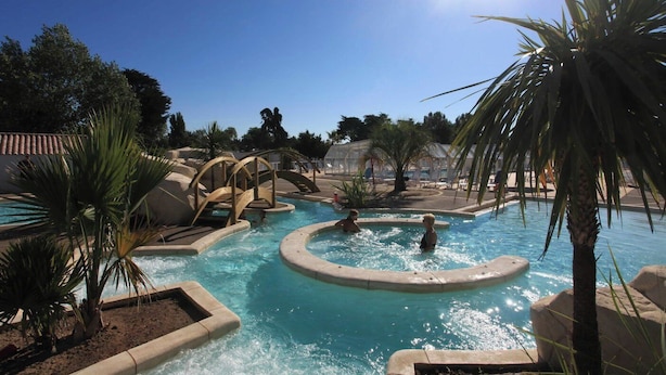 A pool area with multiple water features, including a central fountain and surrounding pools, surrounded by palm trees and lounge chairs. - Domaine du Collet (Les Moutiers-en-Retz)