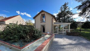 Une maison avec une façade en briques, une véranda en verre et une allée pavée.