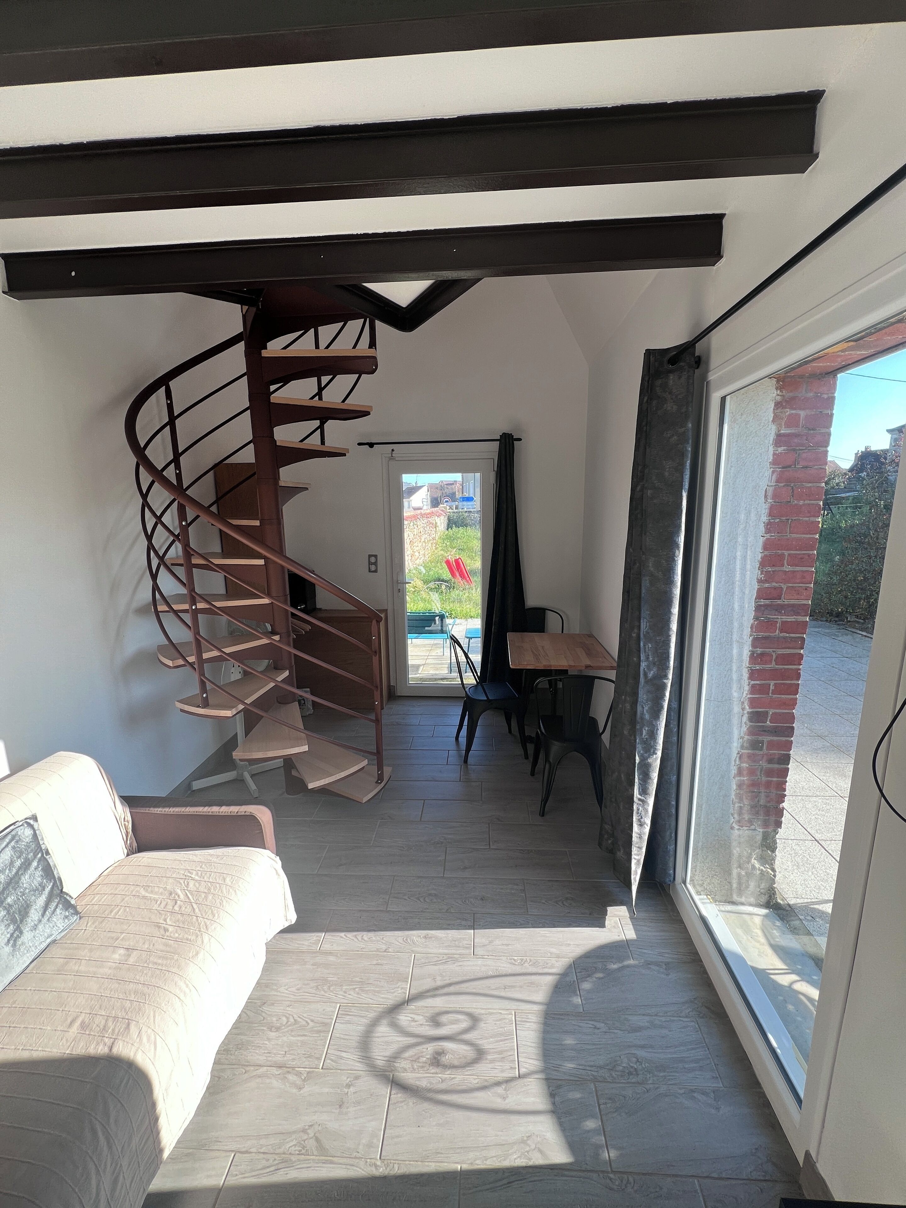 A modern interior with a spiral staircase, a sofa, a dining area, and a large glass door leading outside.