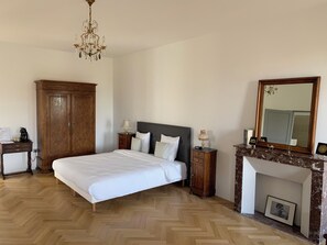 Une chambre à coucher avec un grand lit, une armoire en bois, des tables de chevet, un lustre, une cheminée et un miroir.