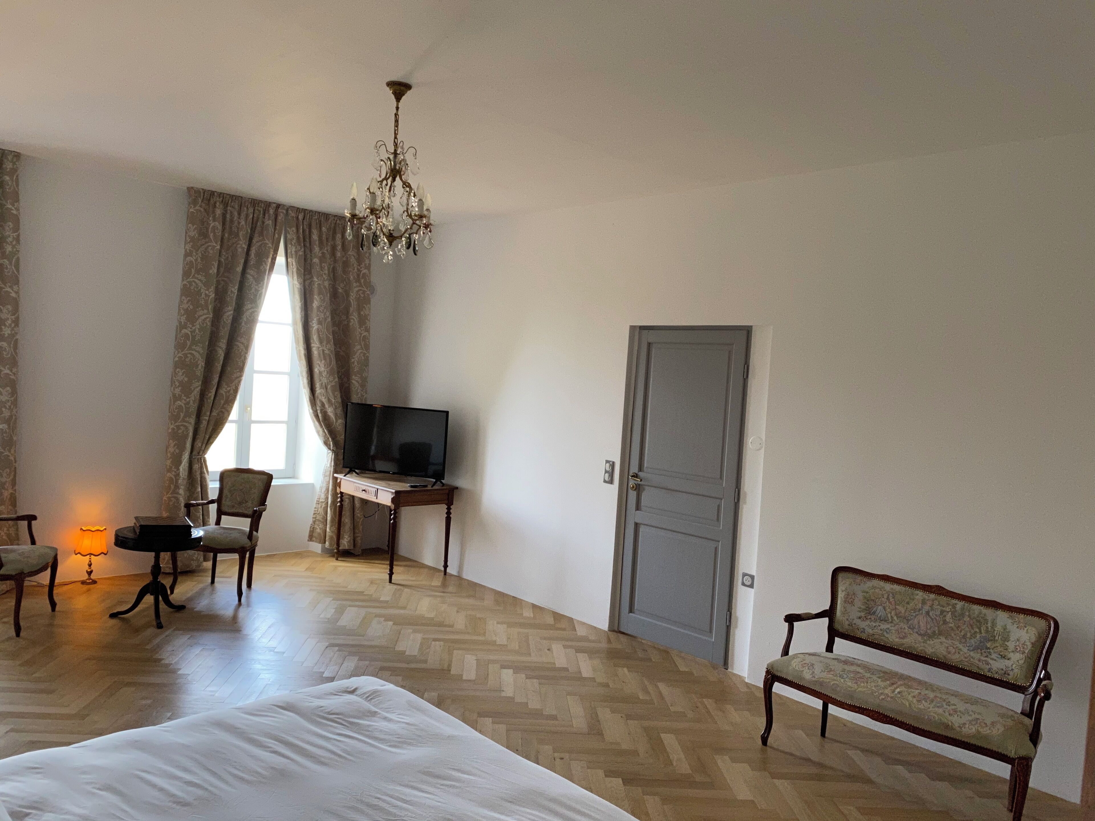 Una habitación de hotel con cama, escritorio con televisor, silla, banco y candelabro.