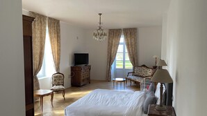 Tilava makuuhuone, jossa on suuri sänky, televisio, puinen lipasto, tuoli, työpöytä ja kattokruunu.