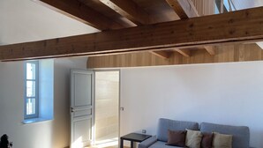 A modern living room with a grey sofa, wooden beams on the ceiling, a small table, and a window with a view. - Thierry room in Château Camus (Montmarault)