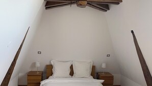 A bedroom with a sloped ceiling, a wooden bed frame, two bedside tables with lamps, and a hanging light fixture. - Thierry room in Château Camus (Montmarault)
