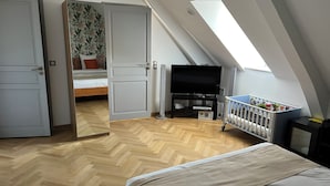 A bedroom with a sloped ceiling, a bed, a TV, a crib, and a door leading to another room. - Jules & Leonard room in Château Camus (Montmarault)