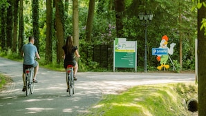 Two people riding bicycles on a paved path surrounded by trees. There is a sign for 'Ruwinkel' and a 'P' parking sign with a duck mascot. - Villa in Scherpenzeel Near Veluwe Forest (Scherpenzeel)
