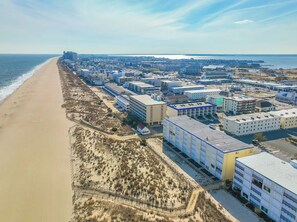 Vista aérea de una ciudad costera con una playa extensa, varios edificios y cielo despejado.