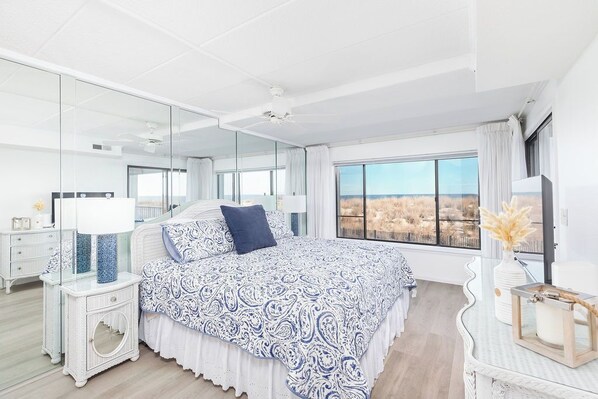 Un dormitorio con una cama grande, una mesita de noche, un espejo y vistas al exterior.