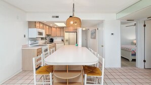 A modern kitchen with white cabinets, a white dining table, and a hanging light fixture.