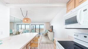 A modern kitchen with a white countertop, a built-in oven, and a microwave. There are wicker chairs and a hanging light fixture.