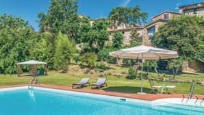 En swimmingpool med solstolar och parasoller, omgiven av grönska och byggnader i sten.