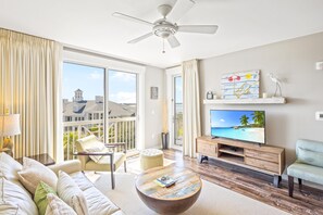 Ein geräumiges Wohnzimmer mit großem Fernseher, bequemen Sitzgelegenheiten und einem Balkon mit Blick.