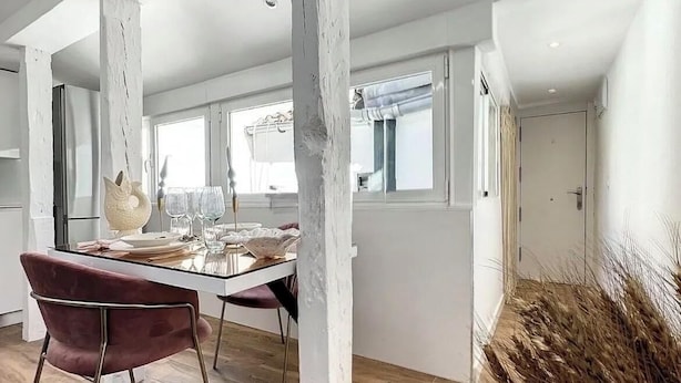 Een ruime kamer met zichtbare houten balken, een eettafel gedekt met borden en glazen, en een rode stoel.