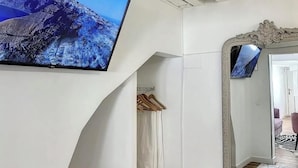 Een kamer met een flatscreen televisie aan een witte muur, een grote spiegel met een sierlijk frame en een houten vloer.