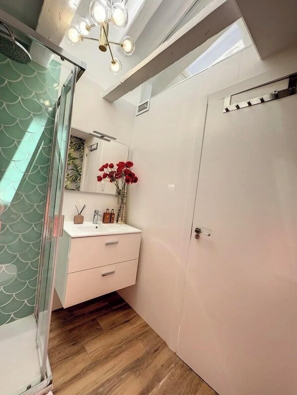 A bathroom with a glass shower enclosure, a white vanity with a mirror, and a door with a towel rack. - Chic Penthouse with Urban Charm & Rooftop (Madrid)