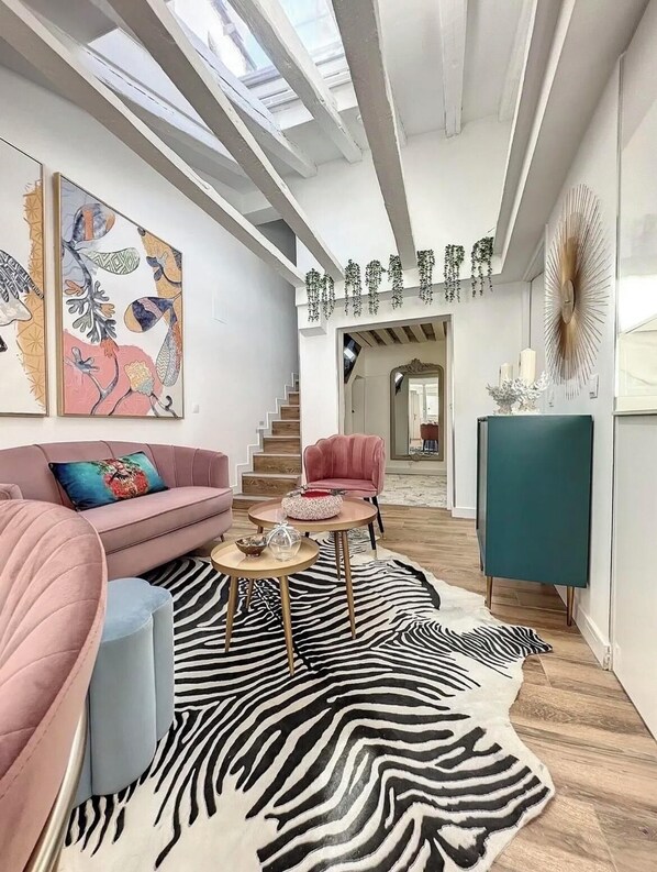 Un salon moderne avec un canapé rose, un tapis à motifs zébrés et un escalier menant à un autre niveau.