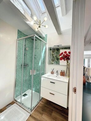 Une salle de bain moderne avec une douche à l’italienne en verre, un meuble-lavabo blanc avec un miroir et une lucarne au plafond.
