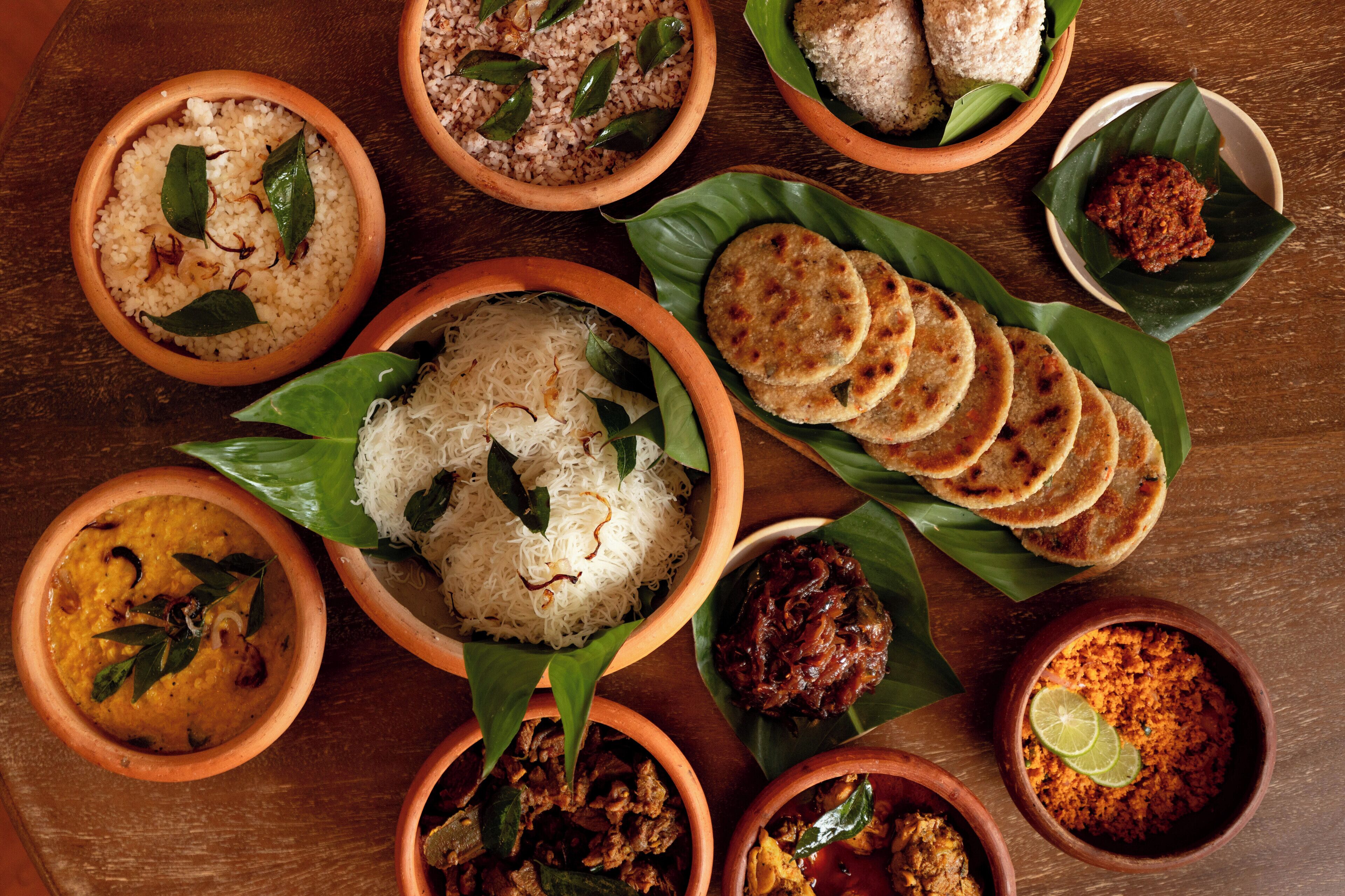 A variety of dishes served on clay plates with banana leaves, including rice, curries, and flatbreads.