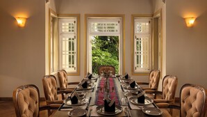 Une salle à manger avec une longue table dressée pour un repas, entourée de chaises, et une fenêtre donnant sur un paysage verdoyant.