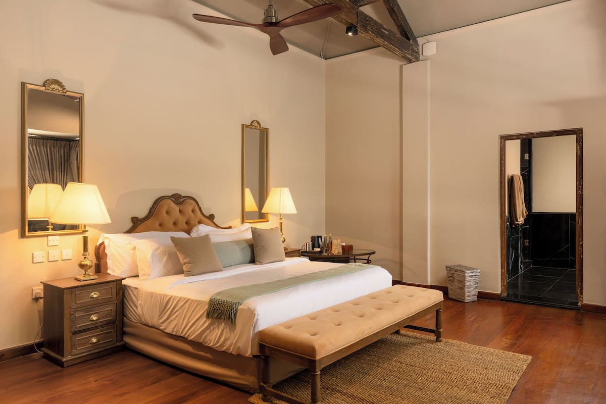 A bedroom with a large bed, two bedside tables with lamps, a ceiling fan, and a mirror on the wall.