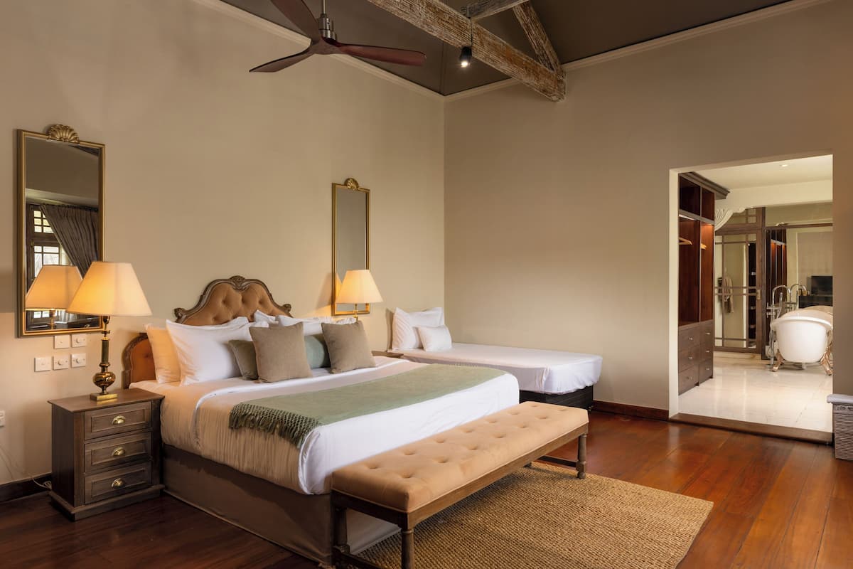 A bedroom with two beds, a wooden bench, a nightstand, and a ceiling fan.