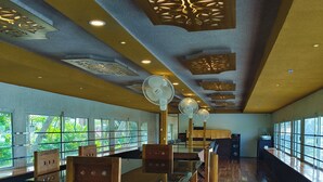 A spacious room with a long wooden table and chairs, large windows, and ceiling fans. - Vinayak House Boats (Alleppey)