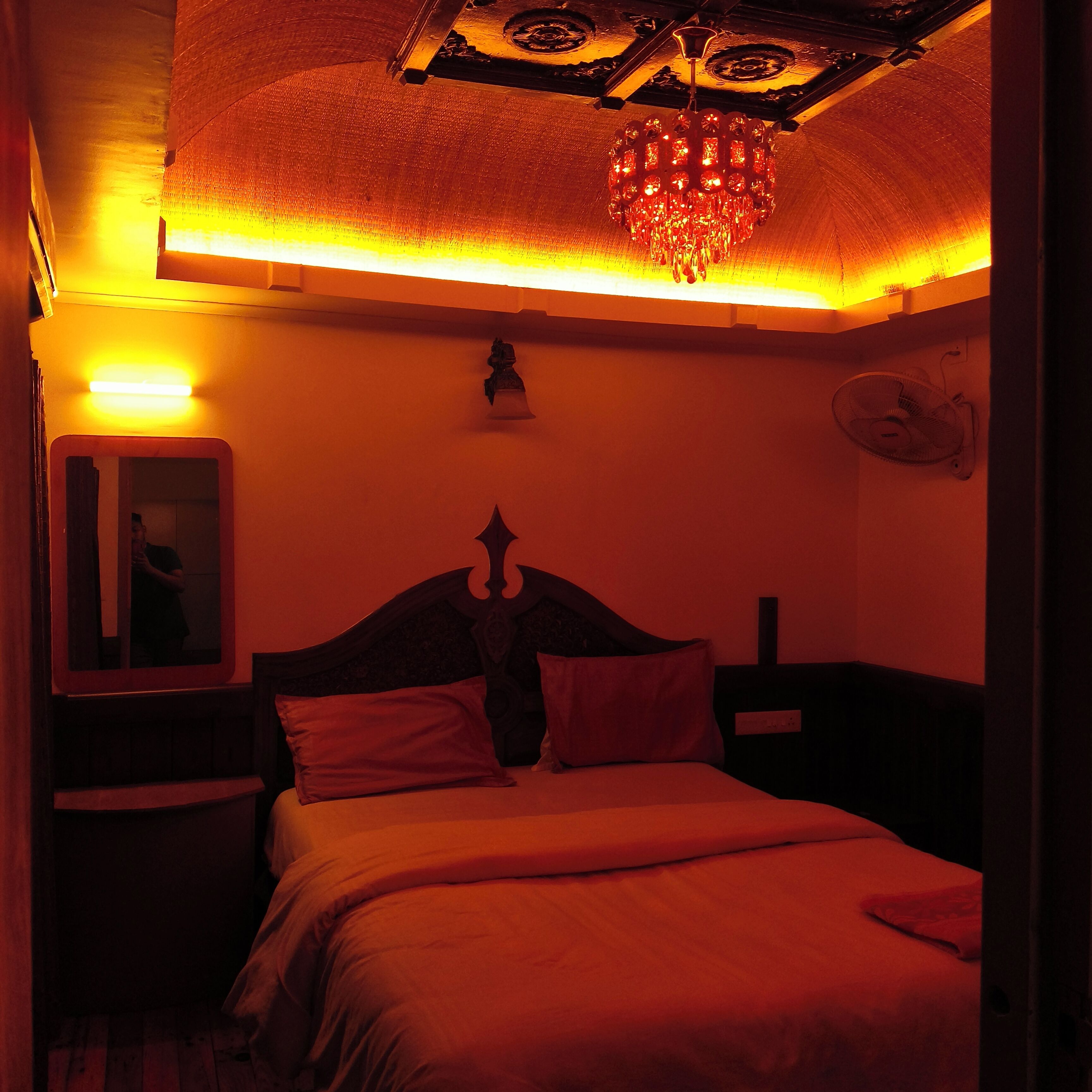 Ein schwach beleuchteter Raum mit einem Bett, einem Spiegel und einer Kristallleuchter.