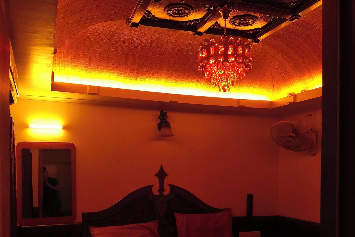 A dimly lit room with a bed, a mirror, and a chandelier.